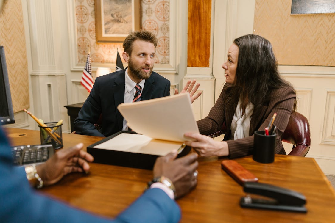 A family law solicitor reviewing documents with a couple across a desk in a professional office, with a bookcase of legal texts in the background