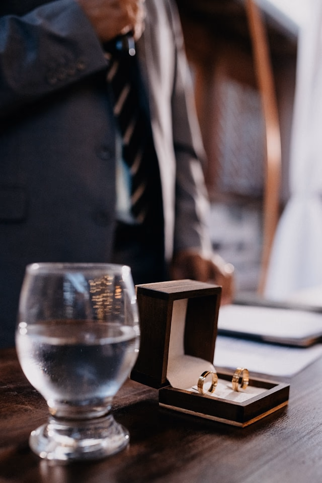 Two wedding rings on an office desk with man in background wearing suit and tie.