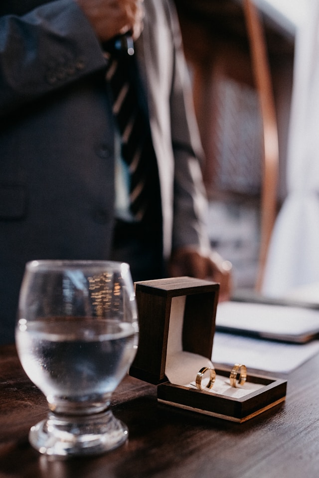 Two wedding rings on an office desk with man in background wearing suit and tie.